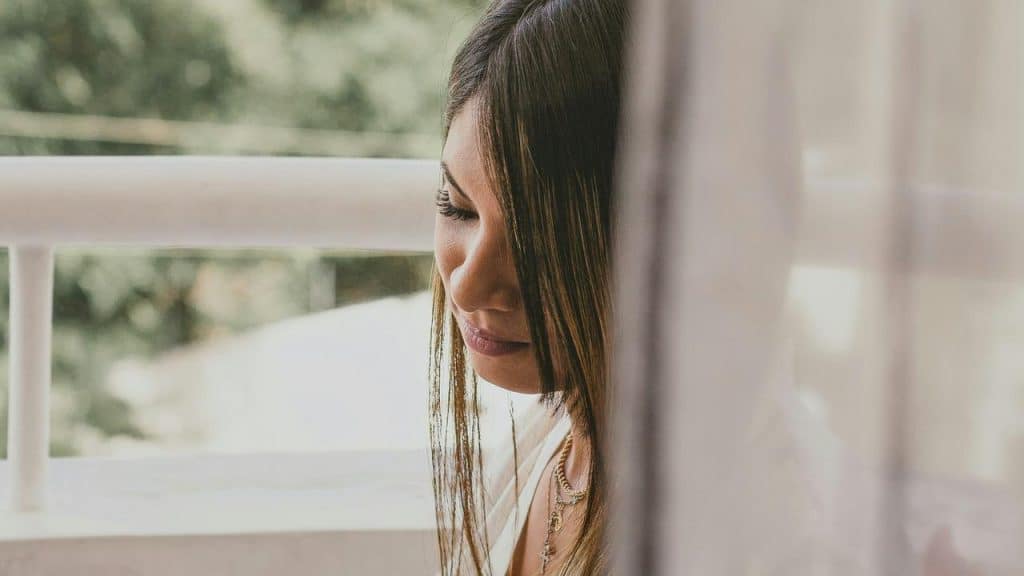 A woman sitting by a window with a soft, thoughtful expression.