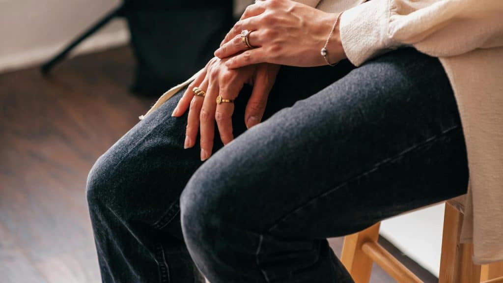 A person sitting with hands resting on their knees, wearing rings and a bracelet.