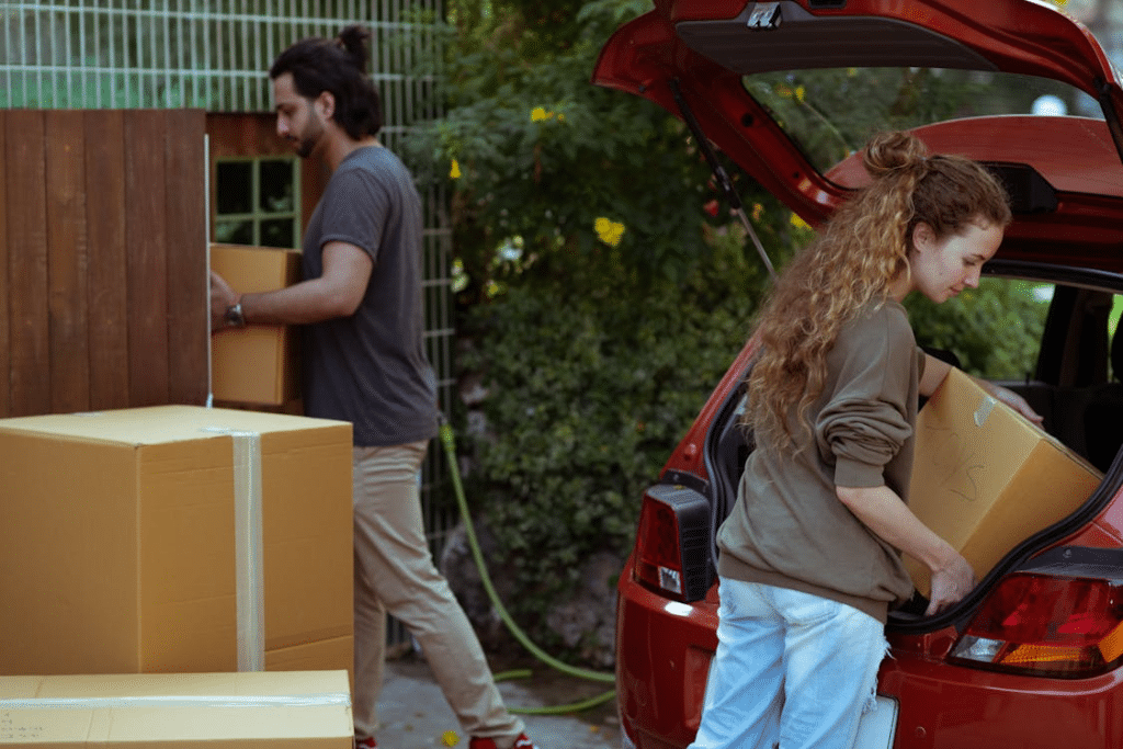 Diverse couple getting carton boxes out of car while relocating in suburb or countryside