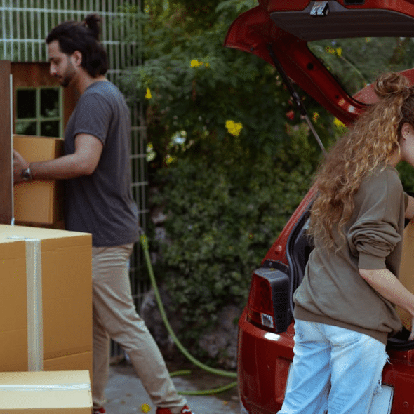 Diverse couple getting carton boxes out of car while relocating in suburb or countryside