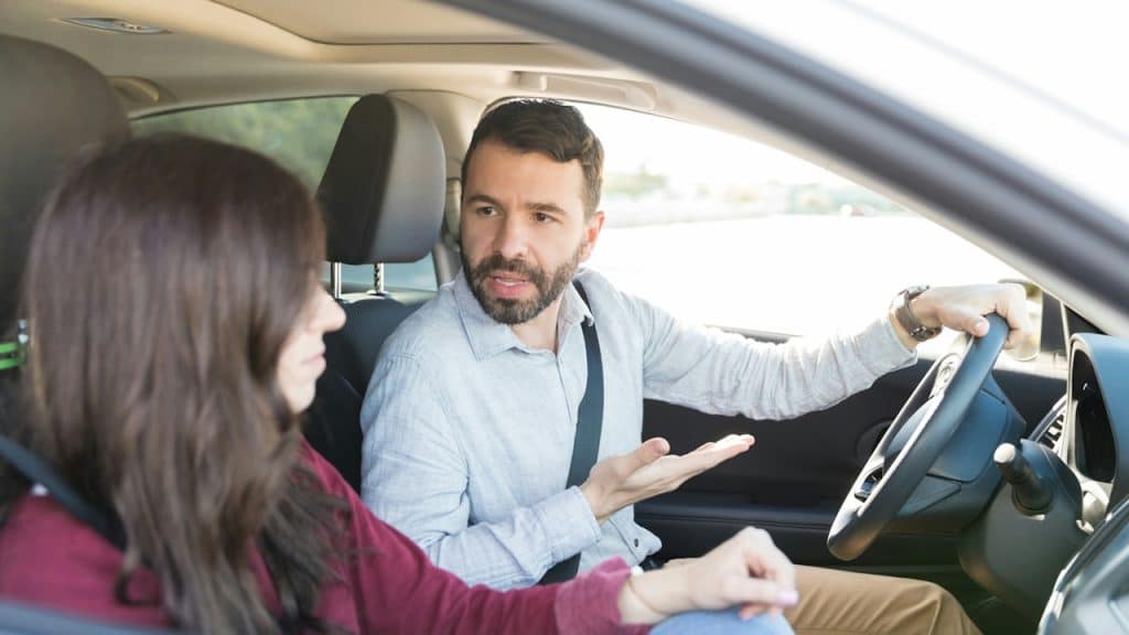 A man driving a car gesturing and looking intensely at a woman in the passenger seat.