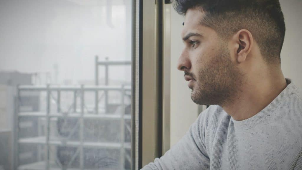 Young man with a short haircut and beard gazing out a large window.