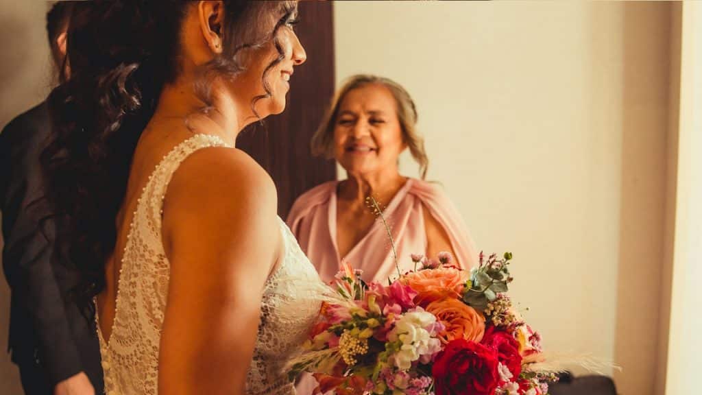 An elderly woman welcoming a newly married couple on entering home.