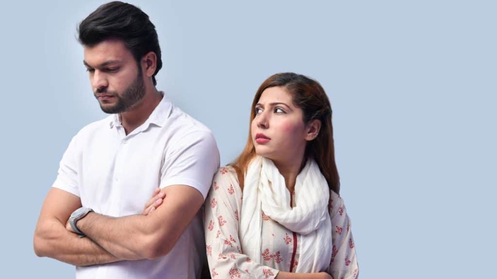 A serious man stands with folded arms next to a woman looking away from him.