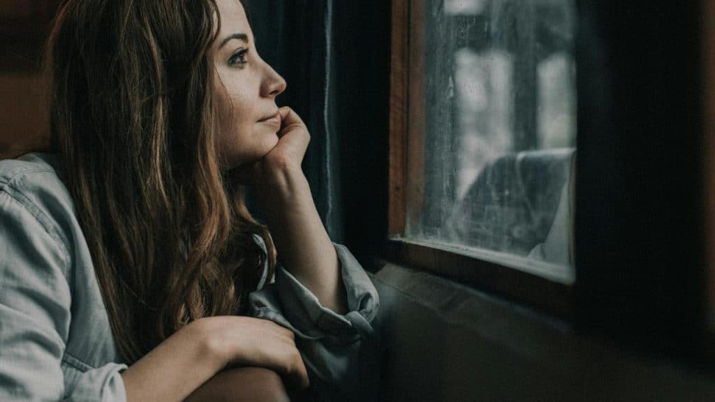 A woman sitting by a window, looking outside thoughtfully.