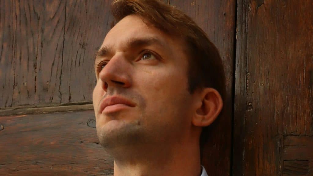 Close-up, low-angle shot of a man looking upward against a textured wooden door.