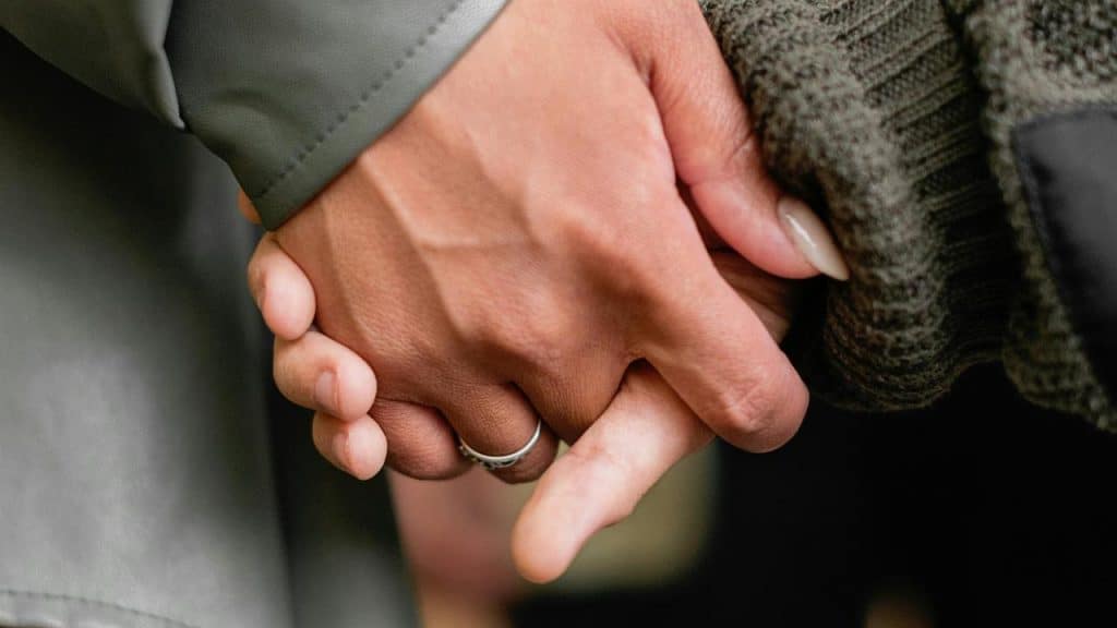 A close-up of two people holding hands while wearing sweaters.