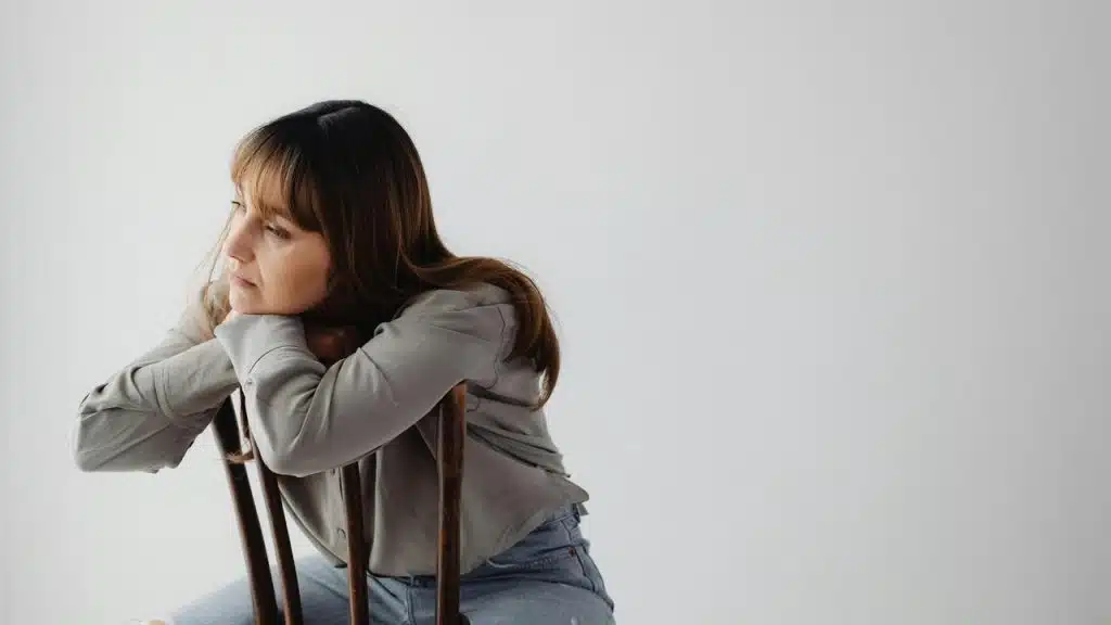A woman sitting backward on a chair resting her chin on the backrest.