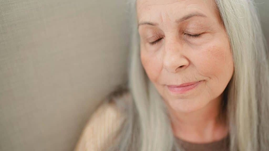 Close-up of an elderly woman with long gray hair and closed eyes.