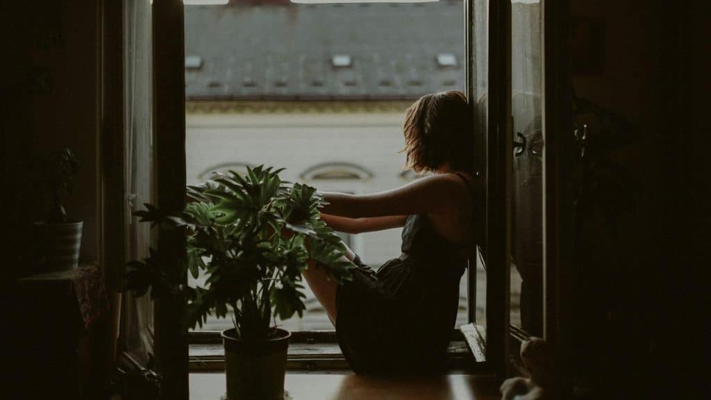 A woman sitting by an open window with plants nearby.