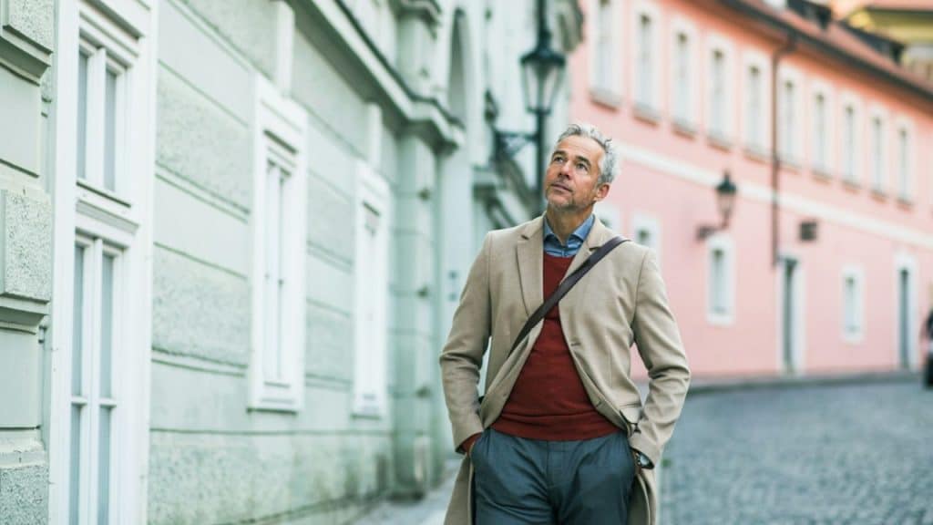 Middle-aged man in a beige coat walking down a European city street.