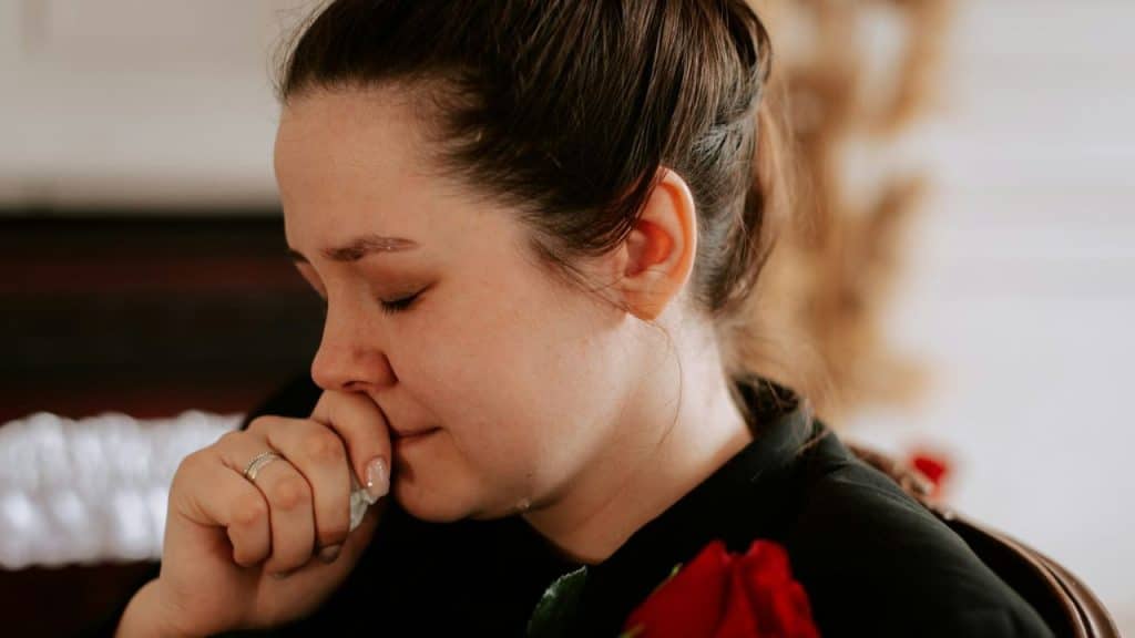 Woman with closed eyes holding a tissue to her face, wearing a black top and a ring.