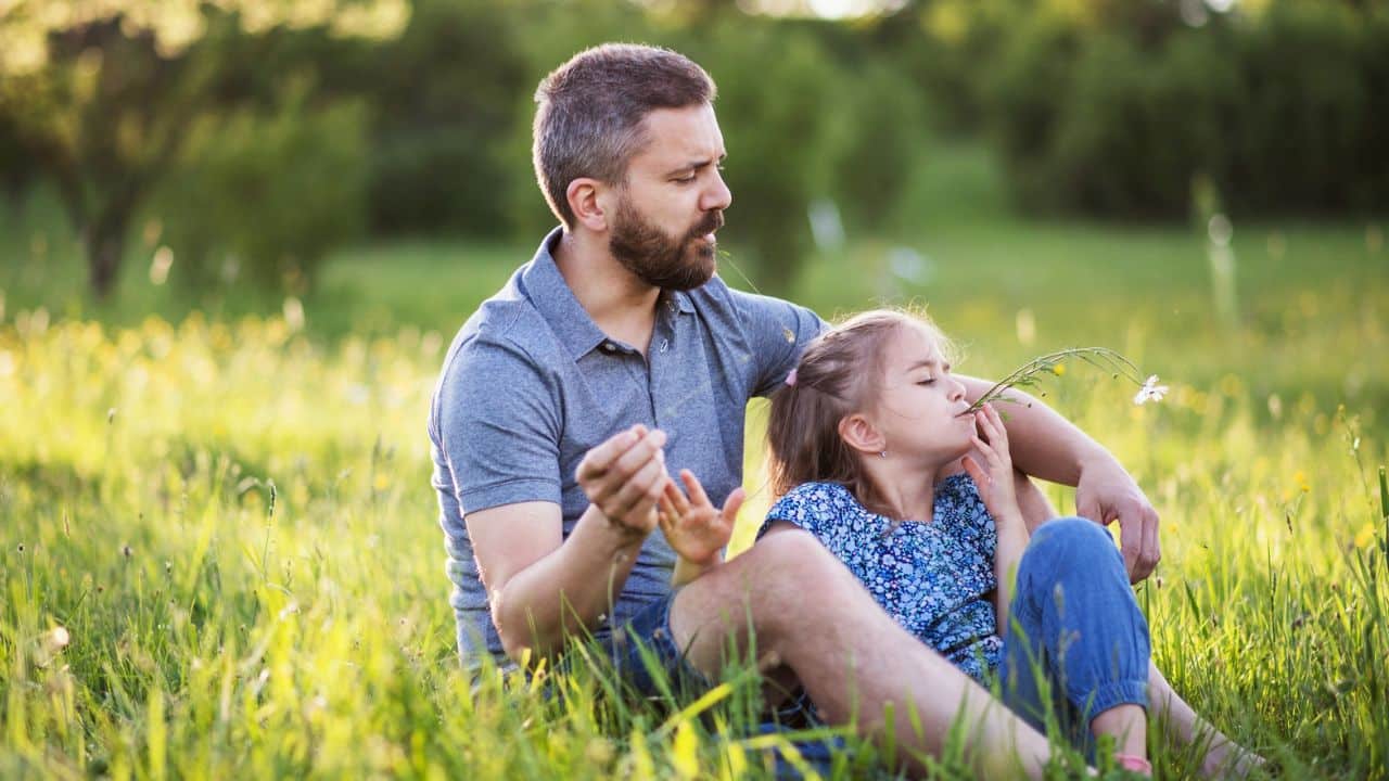 Father and daughter sitting in a grassy field, enjoying the sunny day together.