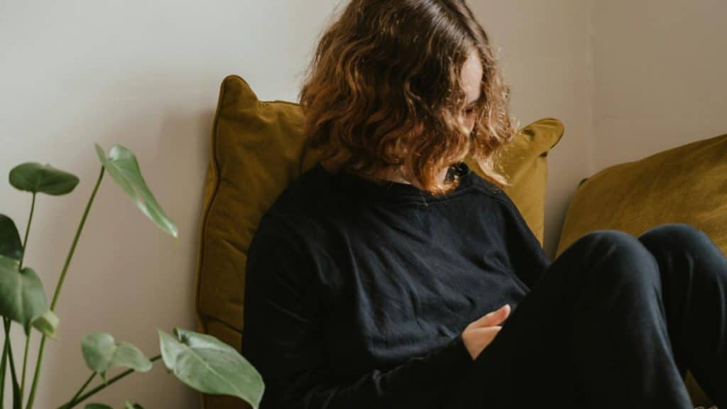 A woman sitting on a couch with her head turned down.