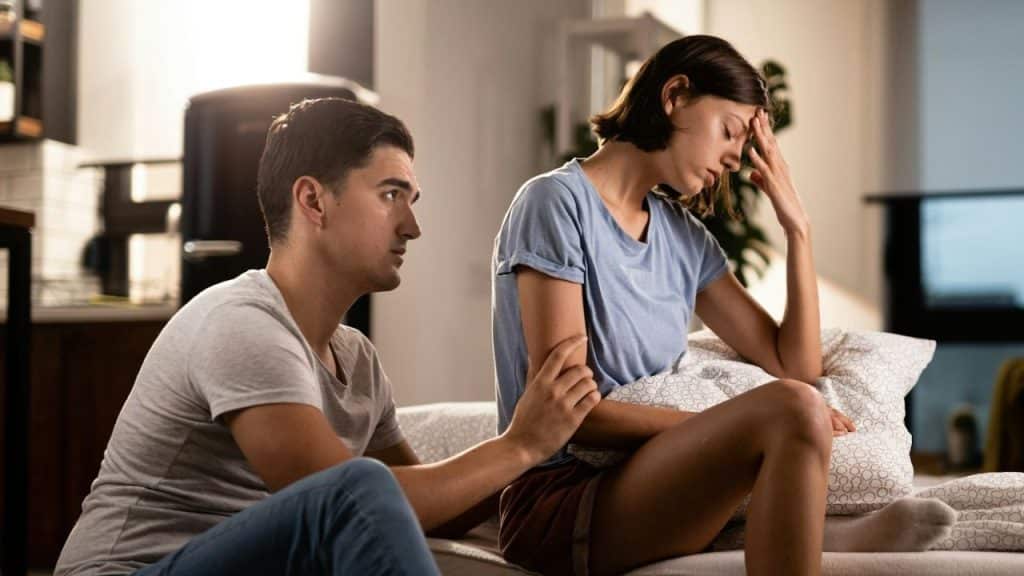 A man trying to comfort a distressed woman sitting beside him on a bed.