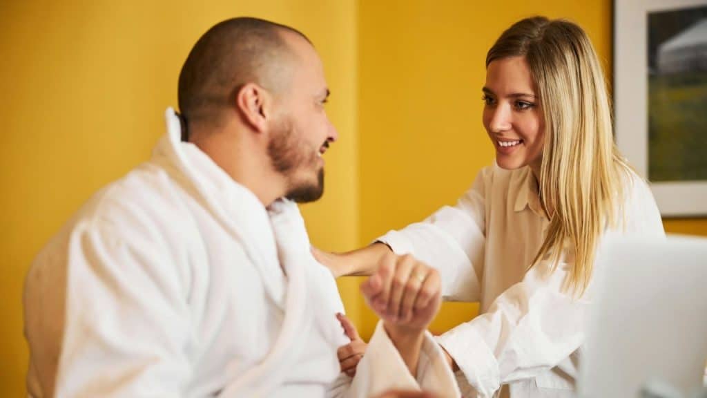 A smiling man in a white robe talks to a woman with blonde hair in a white shirt.
