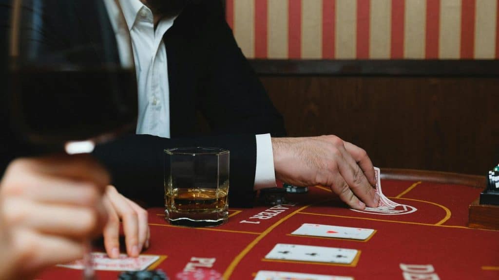 A man in a suit playing cards at a casino table with drinks nearby.