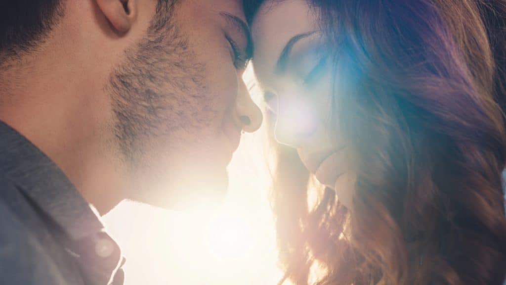 Close-up of a couple forehead-to-forehead with eyes closed and bright sun flare.