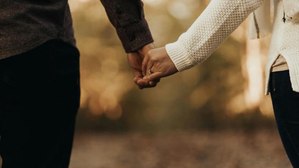 A close-up of two people holding hands outdoors.