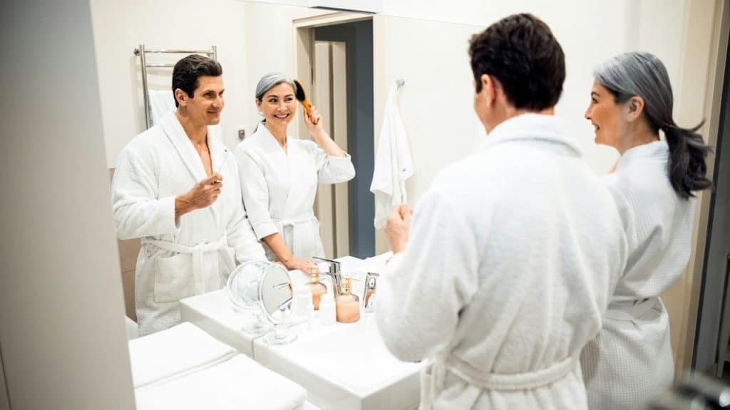 A mature couple in love wearing bathrobes and looking at a mirror in the morning.
