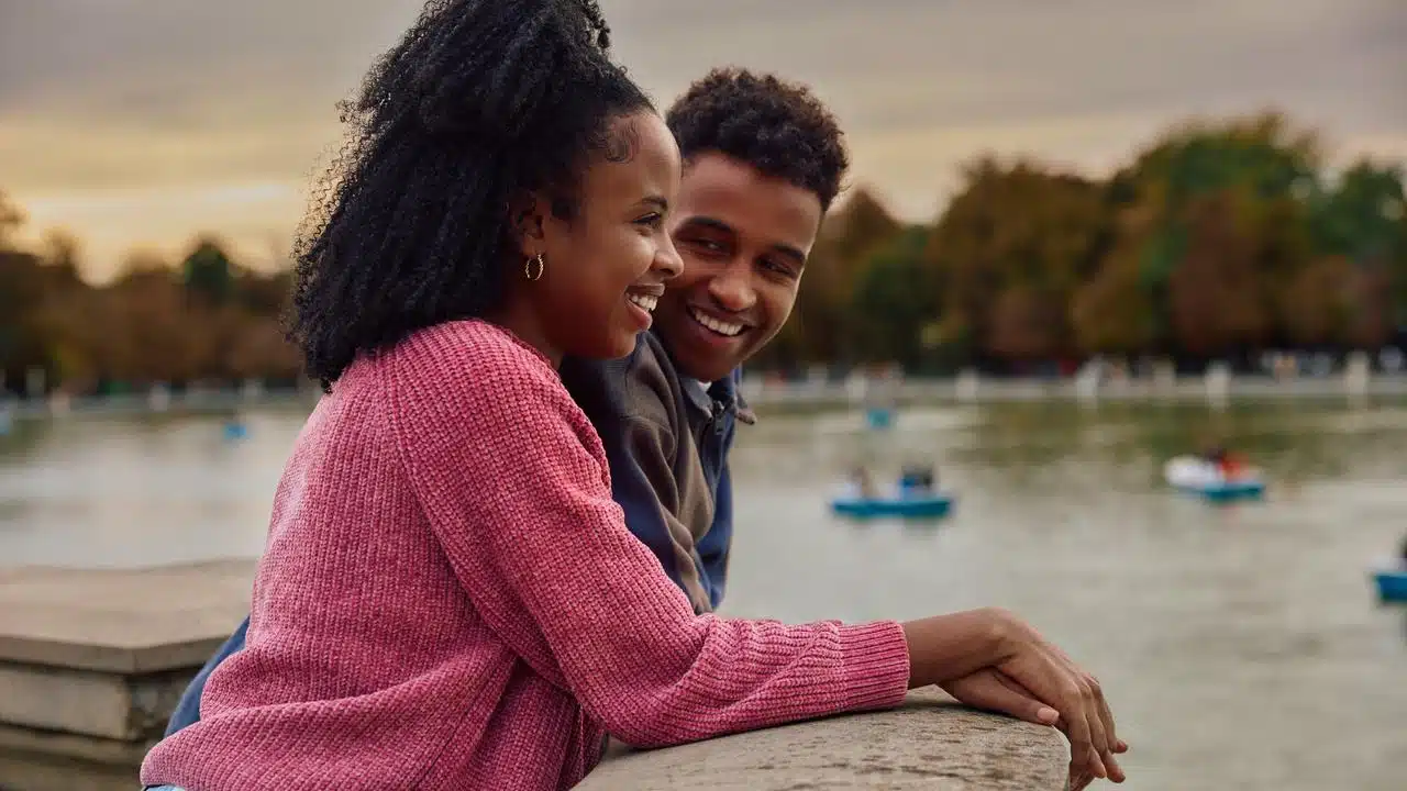 A smiling couple leans on a lakeside railing together at sunset.