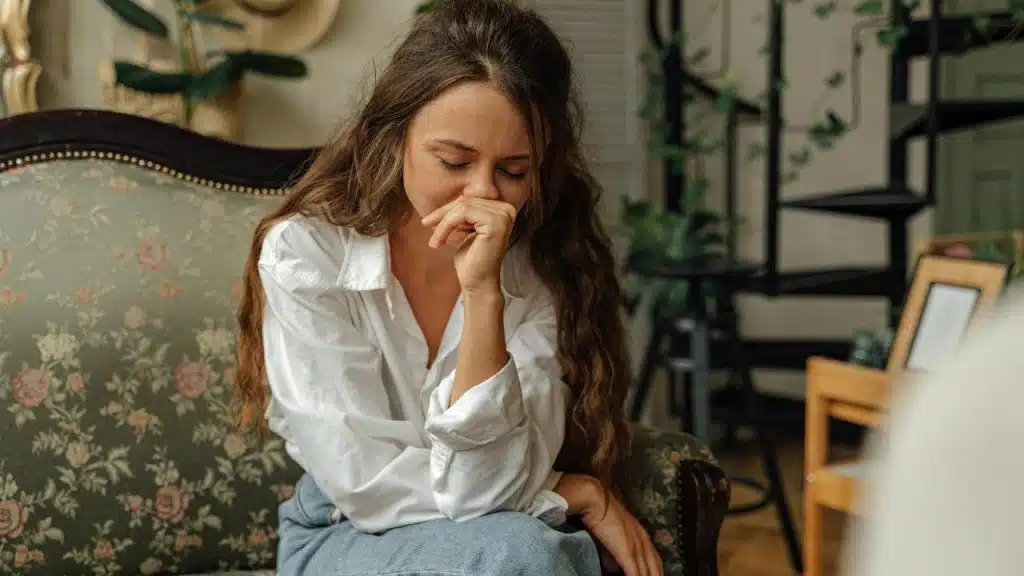 A woman sitting on a couch with her eyes closed, appearing sad or distressed.