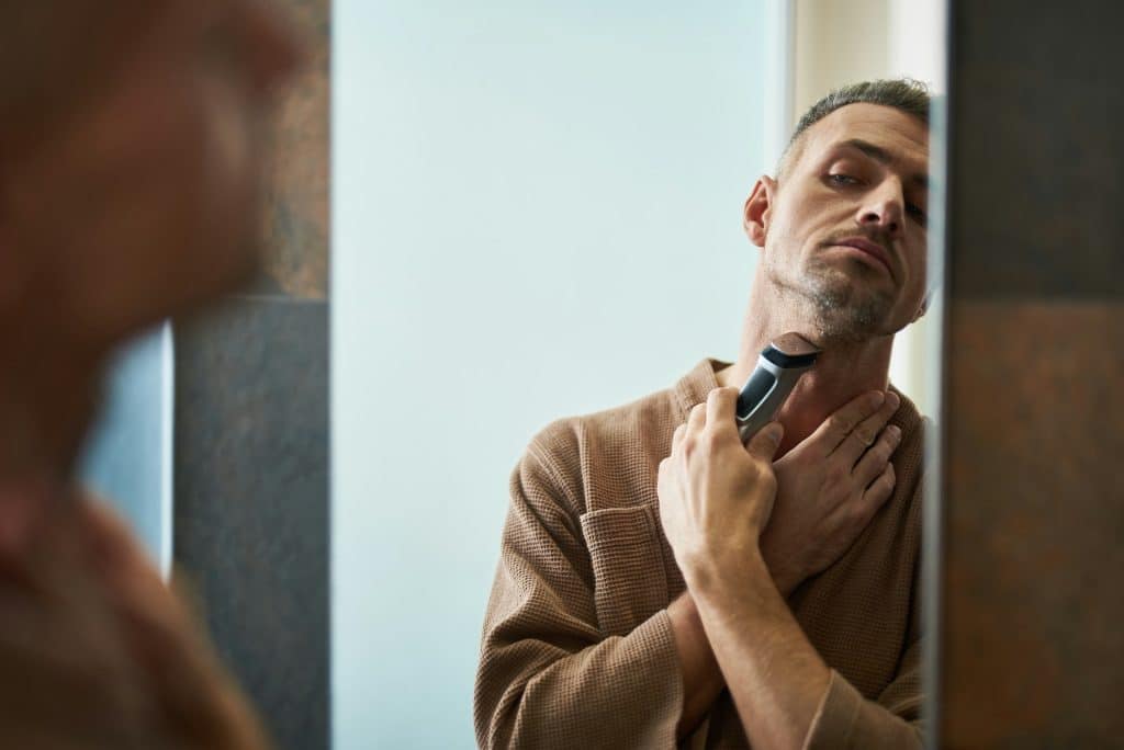A man using an electric shaver while looking at the mirror.