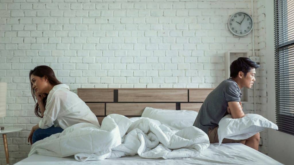 A couple sitting apart from each other on a bed with their backs to each other.