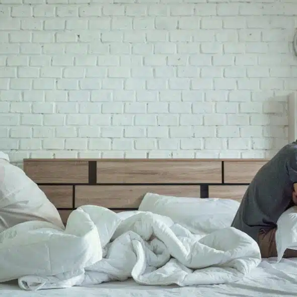 A couple sitting apart from each other on a bed with their backs to each other.