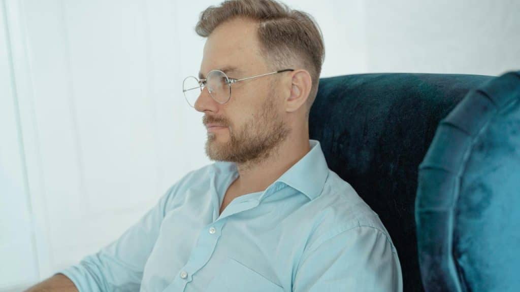 A man in glasses sitting in a chair and looking ahead.
