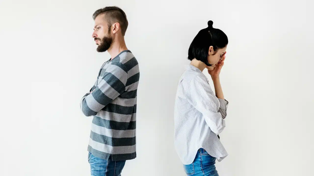 A couple standing with their backs to each other and the woman looking especially melancholic. 
