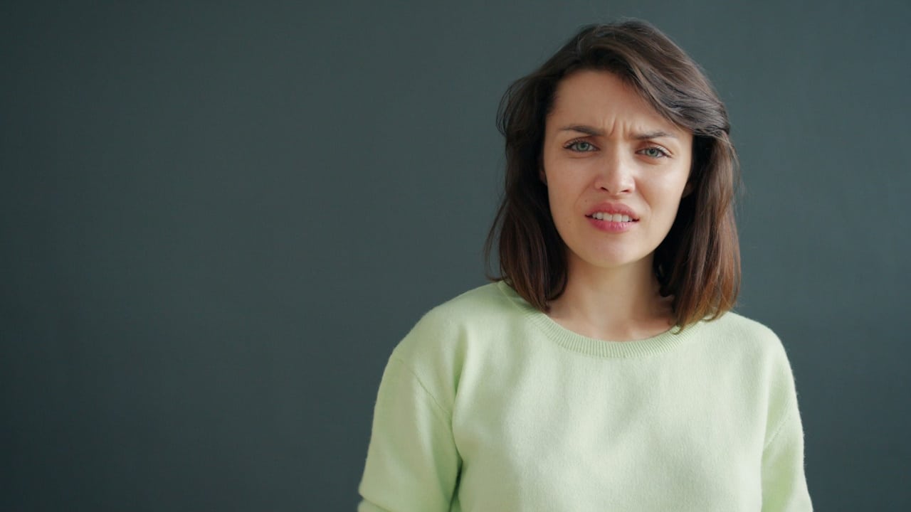 A woman with expressions of disgust is standing against a dark background.