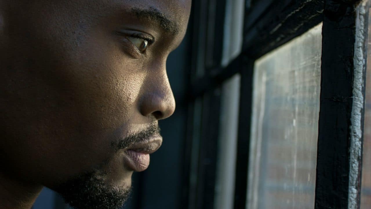 Close-up profile of a man looking out a dark-framed window.