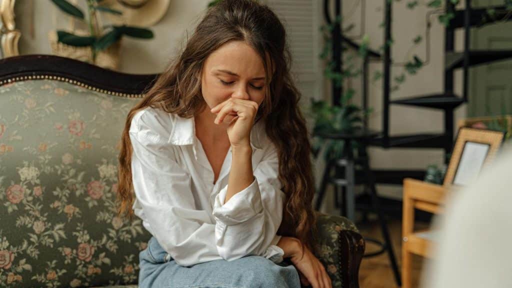 A woman sitting on a couch with her eyes closed, appearing sad or distressed.