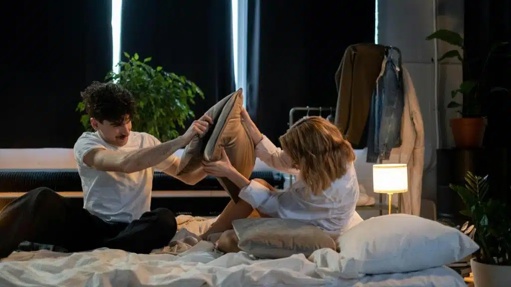 A couple playfully fighting with pillows on a bed.