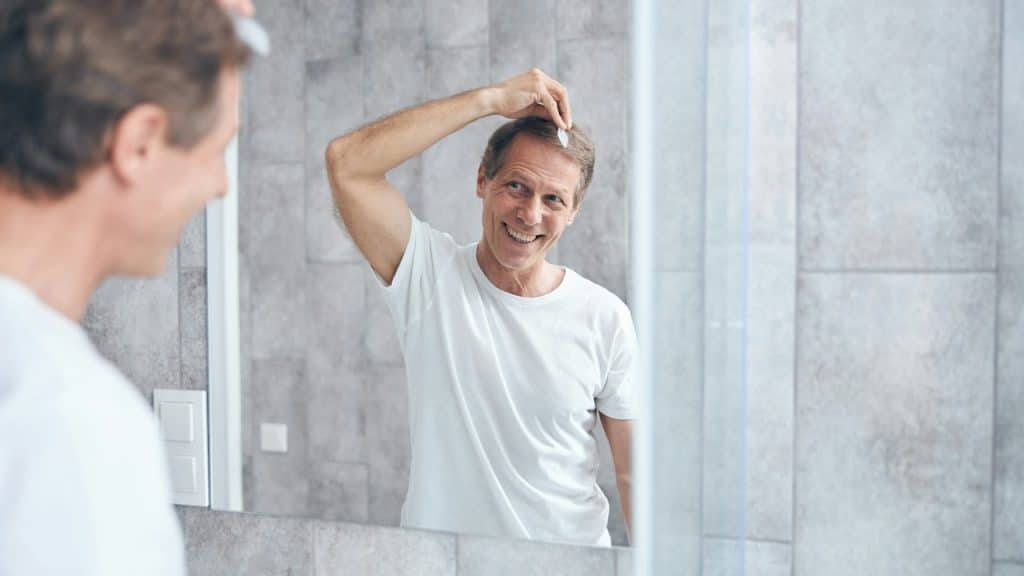 A joyous middle aged handsome caucasian man styling his hair in the bathroom.