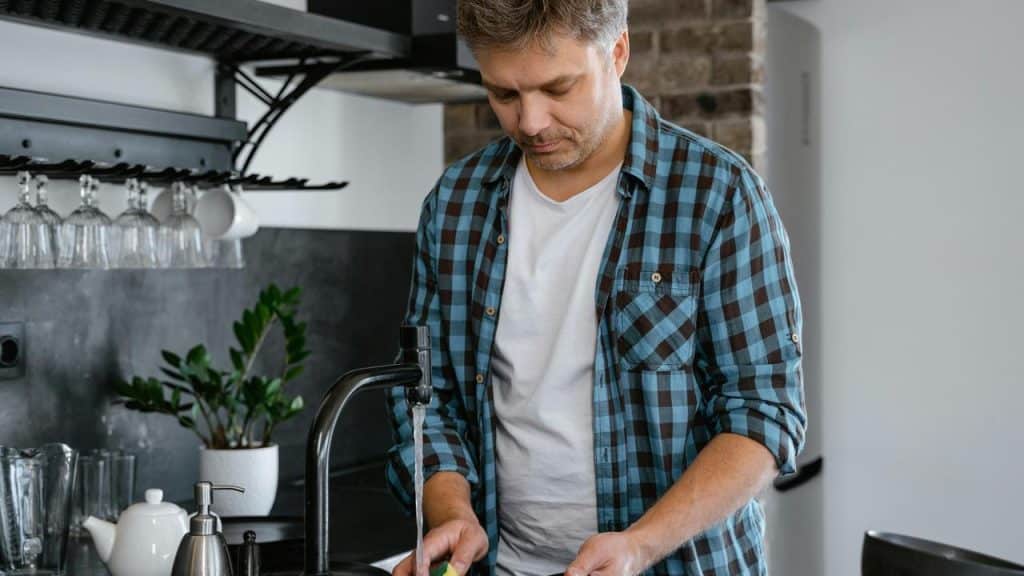 A man washing dishes at a kitchen sink.