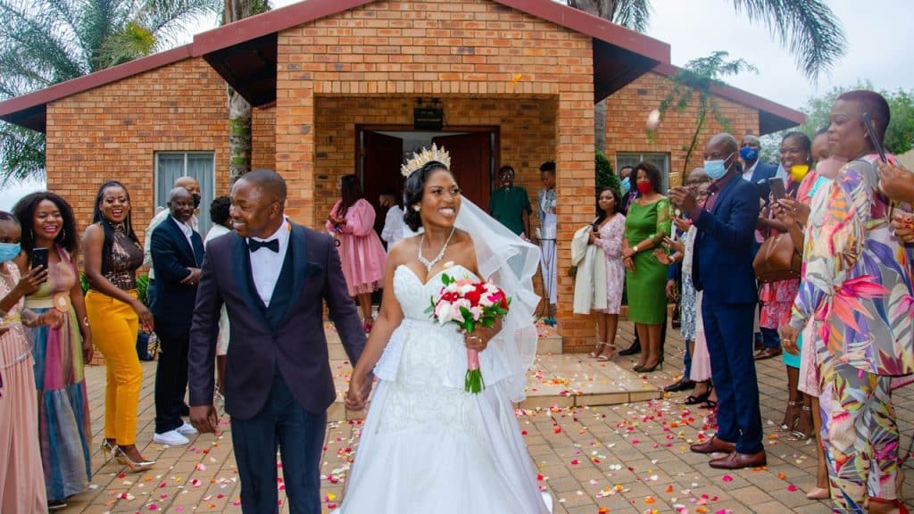 African bride and groom walking down the aisle with guests standing on both sides.