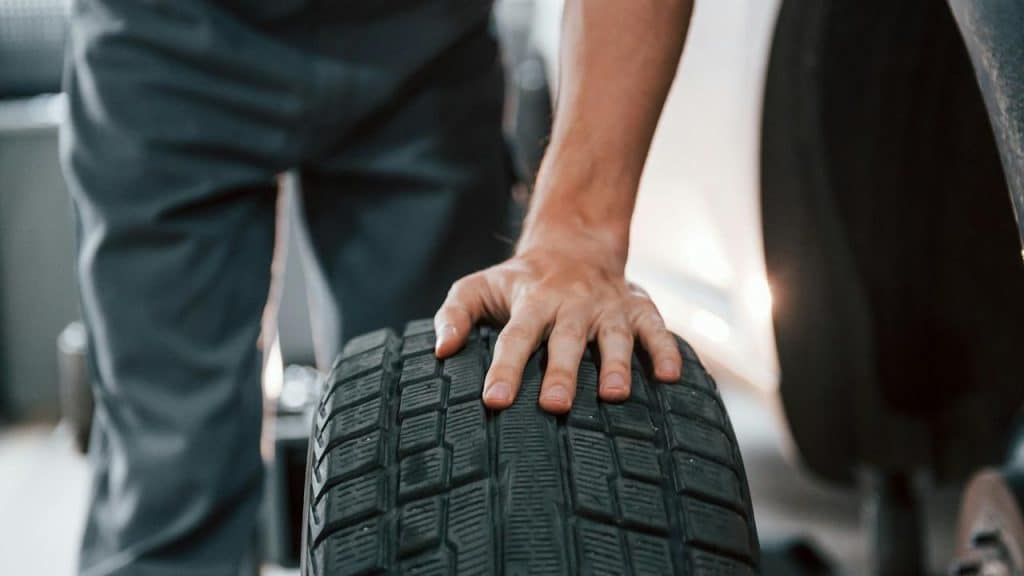 A person holding a car tire during maintenance.