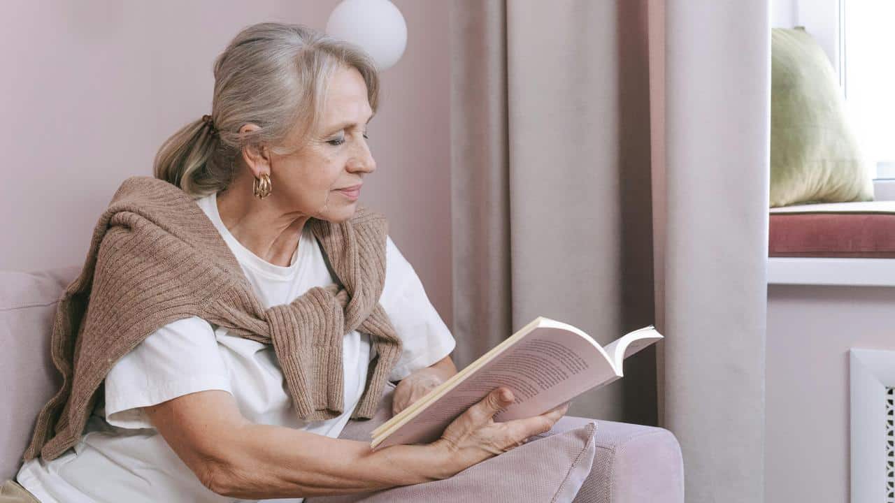An older woman sitting on a couch reading a book.