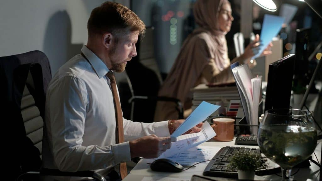 A man and a woman work late at separate desks in a dark office.