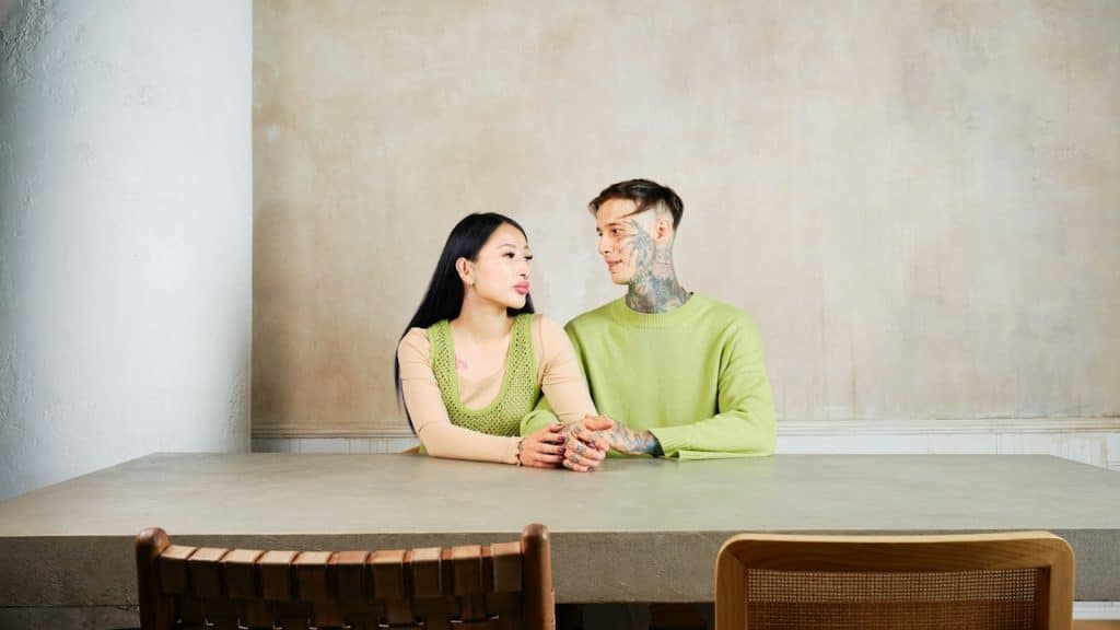 A man with tattoos on face and net is sitting with a woman at a table.