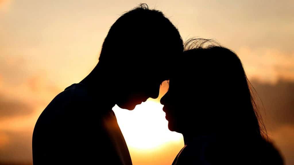 A silhouette of a couple standing forehead to forehead against a bright orange and yellow sunset.