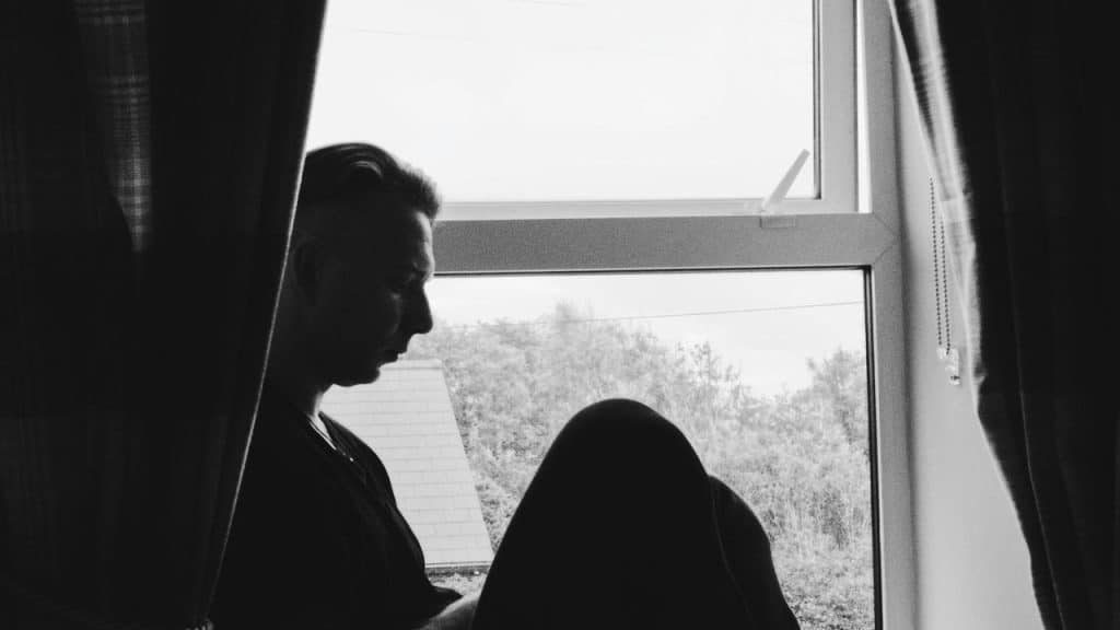 A black-and-white silhouette of a person sitting by a window with curtains.