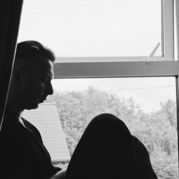 A black-and-white silhouette of a person sitting by a window with curtains.