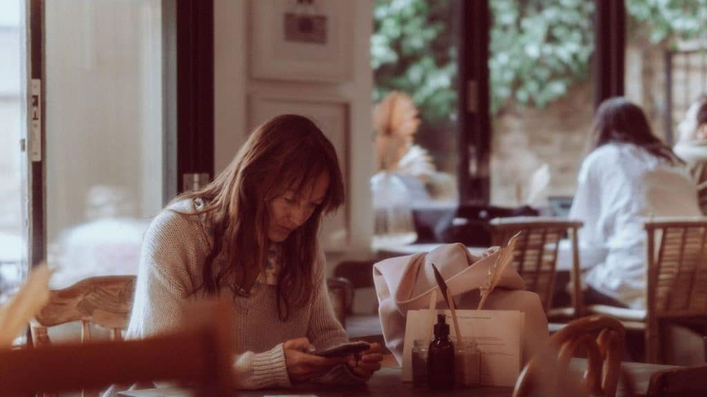 Woman with long hair looking at her phone inside a softly lit cafe.