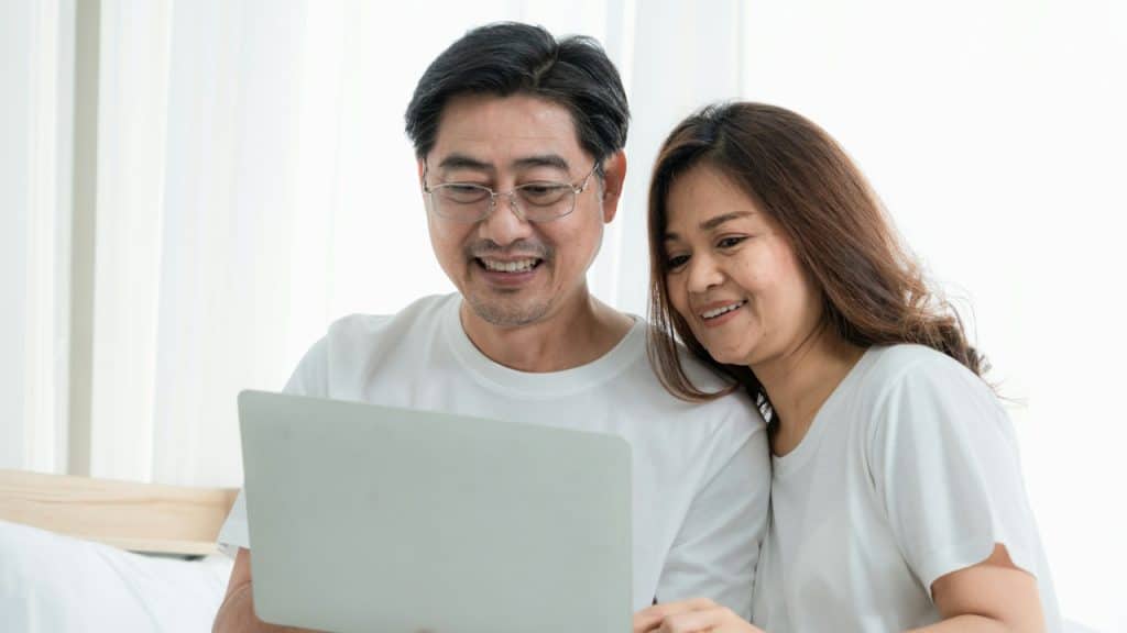 A mature Asian couple looking at a laptop and smiling.