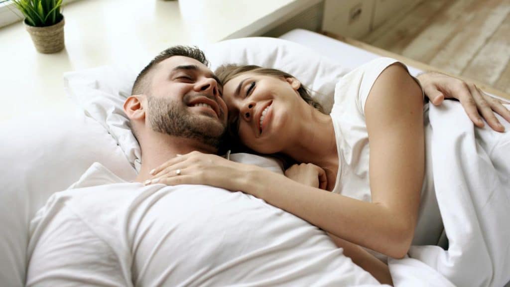 A couple lying in bed smiling and cuddling together.