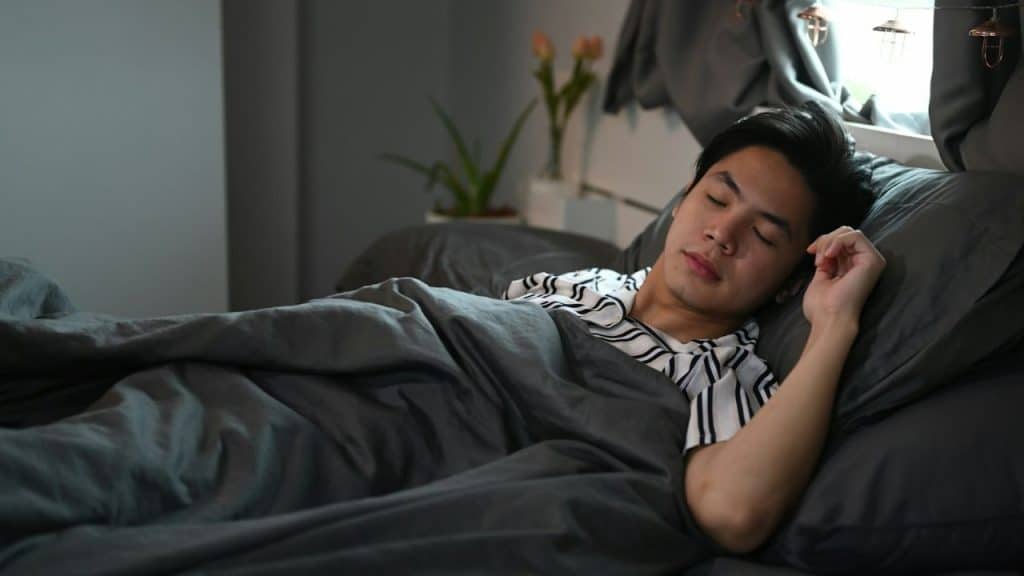 Young man in striped pajamas sleeping in a bed covered with dark gray sheets.
