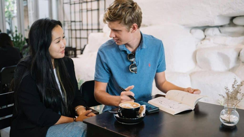 A man and woman talking at a café table with a book and coffee.